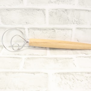 May include: A wooden handled dough whisk with a double loop design. The whisk is made of stainless steel and has a wooden handle.