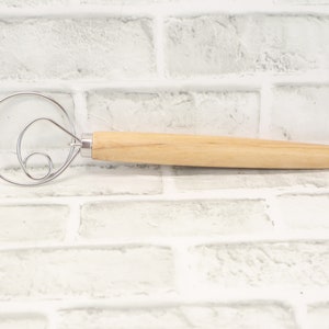 May include: A wooden handled dough whisk with a double loop design. The whisk is made of stainless steel and has a natural wood handle.