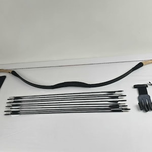 May include: A black recurve bow with a tan handle, a set of black arrows, and archery accessories. The bow is curved and strung, with a leather grip. Accessories include a finger tab and arm guard.
