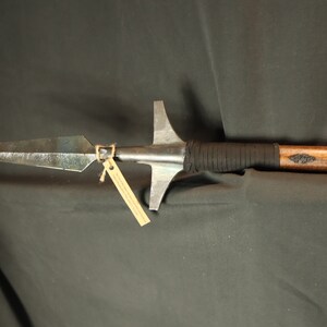 Peut inclure: Une lance artisanale avec une pointe de lance en m&eacute;tal et un manche en bois. La pointe de lance est de forme triangulaire fonc&eacute;e avec une pointe ac&eacute;r&eacute;e. Le manche est envelopp&eacute; d'un mat&eacute;riau noir pr&egrave;s de la t&ecirc;te et comporte un &eacute;l&eacute;ment d&eacute;coratif. Une petite &eacute;tiquette est attach&eacute;e.