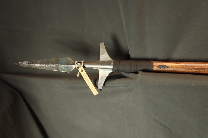 Peut inclure: Une lance artisanale avec une pointe de lance en m&eacute;tal et un manche en bois. La pointe de lance est de forme triangulaire fonc&eacute;e avec une pointe ac&eacute;r&eacute;e. Le manche est envelopp&eacute; d'un mat&eacute;riau noir pr&egrave;s de la t&ecirc;te et comporte un &eacute;l&eacute;ment d&eacute;coratif. Une petite &eacute;tiquette est attach&eacute;e.