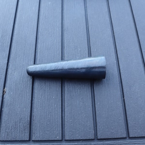 May include: A dark blue, tapered wooden wedge, likely for woodworking or construction. The wedge is lying on a dark blue, grooved surface, possibly a table or deck.