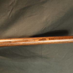 Peut inclure: Gros plan sur une cheville en bois avec une teinture brun fonc&eacute;. La tige est cylindrique et semble &ecirc;tre en bois dur. Le grain du bois est visible et la tige a une finition lisse.