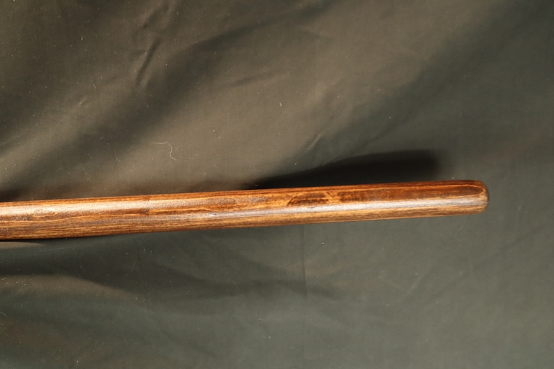Peut inclure: Gros plan sur une cheville en bois avec une teinture brun fonc&eacute;. La tige est cylindrique et semble &ecirc;tre en bois dur. Le grain du bois est visible et la tige a une finition lisse.