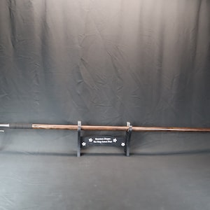 May include: A wooden spear with a metal tip, mounted on a black stand with a white inscription that reads "Custom Weapon The King's Medieval Shop".