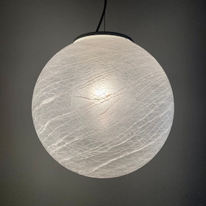 May include: A spherical pendant light with a textured, white glass shade. The shade features a cracked, web-like pattern and hangs from a black cord. The light is illuminated internally, producing a soft glow.