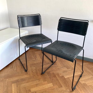 May include: Two black metal chairs with black woven seats. The chairs are on a wooden floor.