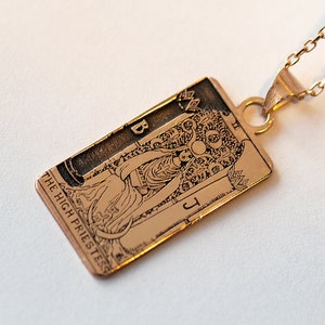 Op de afbeelding: Een gouden ketting met een hanger met de tarotkaart Hogepriesteres. De hanger is rechthoekig en heeft een gedetailleerd beeld van de traditionele symboliek van de kaart.