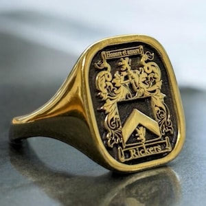 Peut inclure: Une chevalière dorée avec un blason gravé. Le blason présente un écusson, des ornements et l'inscription "Honore et amore" en haut. Le nom "Rickers" est inscrit en bas du blason.