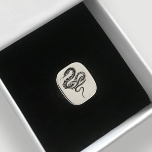 May include: A silver ring with a black snake design in a white box with a black interior.
