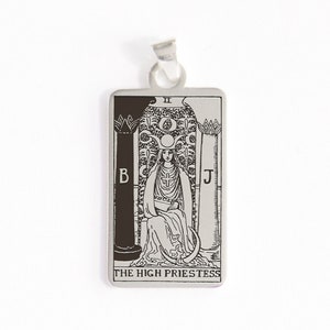 Op de afbeelding: Zilveren hanger met een zwart-witte illustratie van de tarotkaart Hogepriesteres. De kaart toont een vrouw die op een troon zit met een halve maan boven haar hoofd. De kaart wordt omlijst door twee pilaren met de letters B en J erop. De tekst "THE HIGH PRIESTESS" staat onderaan de kaart gedrukt.