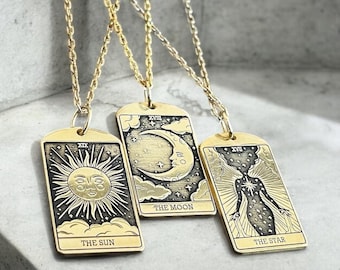 May include: Three gold necklaces with pendants featuring tarot card imagery. The pendants depict The Sun, The Moon, and The Star cards. Each pendant has a Roman numeral and the card name.