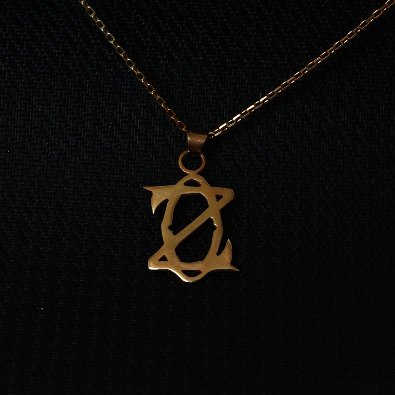 May include: A gold chain necklace with a pendant featuring a stylized letter 'Z' design.