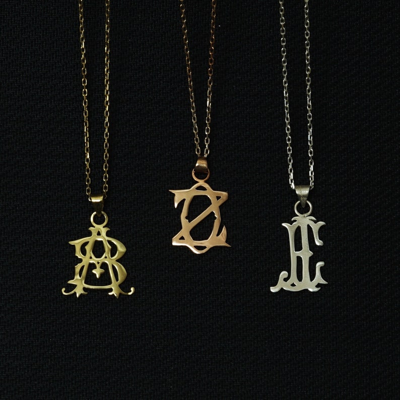 May include: Three gold necklaces with different initial pendants. The pendants are in the shape of the letters A, Z, and E. The necklaces are on a black background.