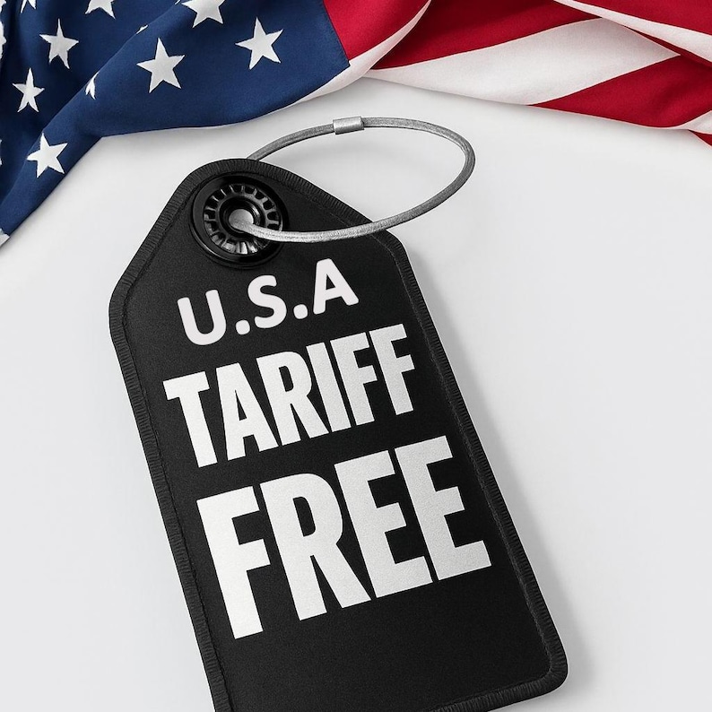 May include: A black tag with the text "U.S.A TARIFF FREE" in white, with a silver metal loop. The tag is set against a backdrop of the American flag, with its red and white stripes and blue field with white stars.