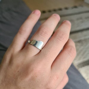 Puede incluir: Un anillo de plata con un dise&ntilde;o &uacute;nico y asim&eacute;trico. El anillo se lleva en un dedo.