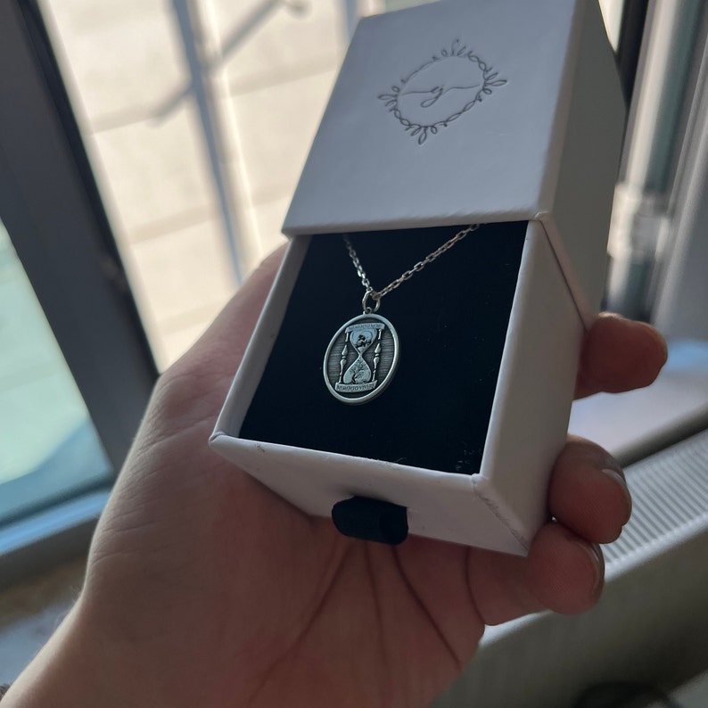 Pu&ograve; includere: Una collana d'argento con un ciondolo a forma di clessidra. Il ciondolo &egrave; inciso con la parola "remarkable".