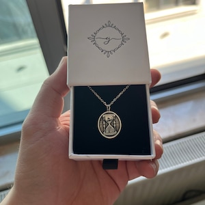 Pu&ograve; includere: Una collana d'argento con un ciondolo ovale che presenta un design a clessidra e l'iscrizione "Il tempo non aspetta nessuno". La collana &egrave; in una scatola bianca con un interno nero.