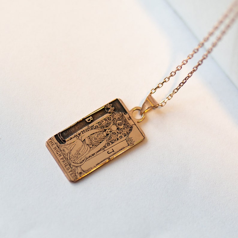 Op de afbeelding: Een gouden ketting met een hanger met de tarotkaart Hogepriesteres. De hanger is rechthoekig en heeft een gedetailleerd beeld van de traditionele symboliek van de kaart.