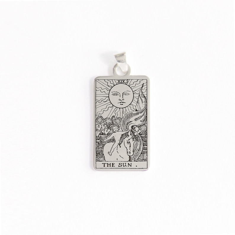 May include: A silver pendant featuring a tarot card design. The card depicts the Sun card, with the Roman numeral XIX at the top and the words "THE SUN." at the bottom.