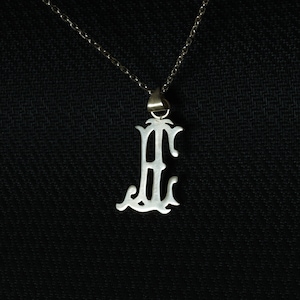 May include: A silver chain necklace with a pendant in the shape of the letter "E". The pendant is ornate and has a decorative design.