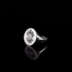 May include: A silver signet ring with a round face featuring a detailed engraving of Medusa's head with snakes for hair.
