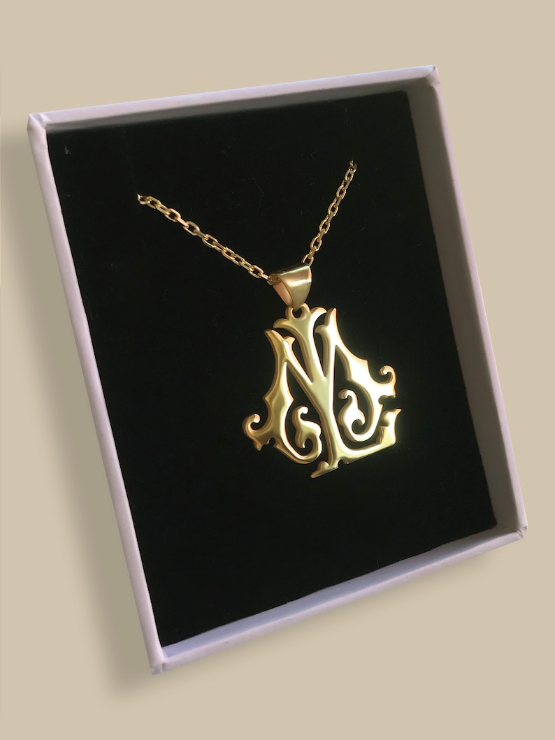 May include: A gold-colored necklace with a pendant featuring a stylized letter 'N' and 'Y' design. The necklace is displayed in a white box with a black velvet interior.