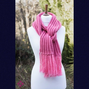 May include: A pink knitted scarf with fringe on the ends. The scarf is tied in a knot and draped over a white mannequin.