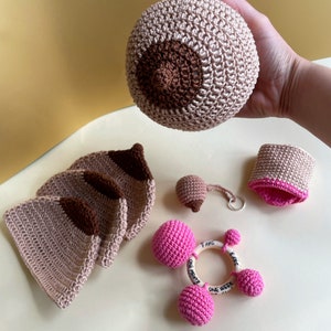 May include: A set of crocheted baby toys in pink and brown. The set includes a rattle, a teether, and a pair of booties. The toys are made with soft yarn and are perfect for babies to explore and play with.