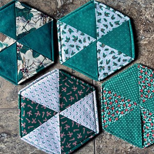 May include: Four green and white hexagon-shaped quilted pot holders with different Christmas-themed patterns.