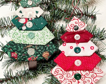 May include: Two fabric ornaments shaped like Christmas trees, each constructed from stacked, folded fabric layers in green and red patterns, secured with white and green buttons, and featuring a brown ribbon trunk at the base.