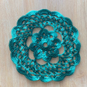 Puede incluir: Un encaje de ganchillo verde y azul con un diseño floral en el centro.