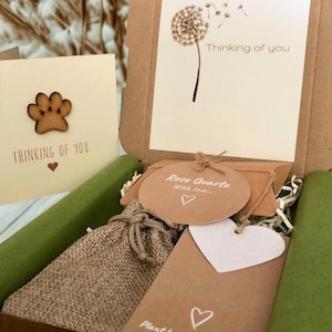 May include: A brown cardboard gift box containing a burlap drawstring pouch, a round tag labeled Rose Quartz With love, a white heart-shaped tag, and a card with a dandelion illustration and the text Thinking of you, plus a separate paw print card.