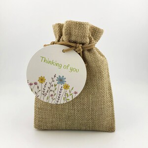 May include: A small burlap bag with a round tag that says "Thinking of you" and has a floral design.