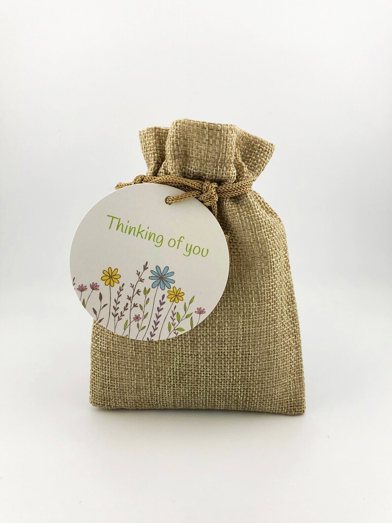 May include: A small burlap bag with a round tag that says "Thinking of you" and has a floral design.
