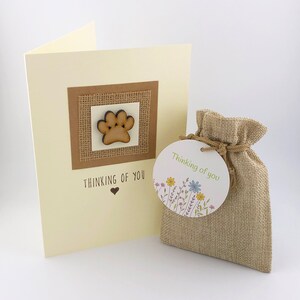 May include: A sympathy card with a wooden paw print on a burlap background. The card says "Thinking of you" with a heart. A small burlap bag with a tag that says "Thinking of you" with flowers.
