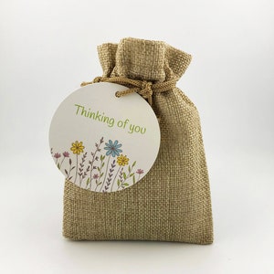 Op de afbeelding: Een klein jute zakje met een rond label waarop "Thinking of you" staat en dat een bloemenmotief heeft.