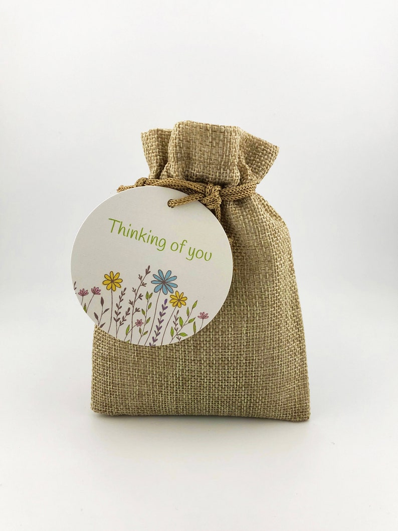 Op de afbeelding: Een klein jute zakje met een rond label waarop "Thinking of you" staat en dat een bloemenmotief heeft.