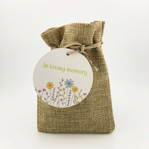 May include: A small burlap bag with a round tag that says "In loving memory" with a floral design.