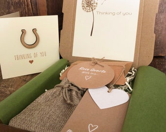 May include: A brown cardboard box with a green tissue paper lining. The box contains a small burlap bag, a card with the text "Rose Quartz With love..." and a card with the text "Plant happy memories..." The box also includes a card with a dandelion and the text "Thinking of you".