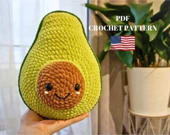 Könnte beinhalten: Ein gehäkeltes Avocado-Kissen mit einem lächelnden Gesicht. Das Kissen ist grün und braun und hat eine strukturierte Oberfläche. PDF-Häkelanleitung.