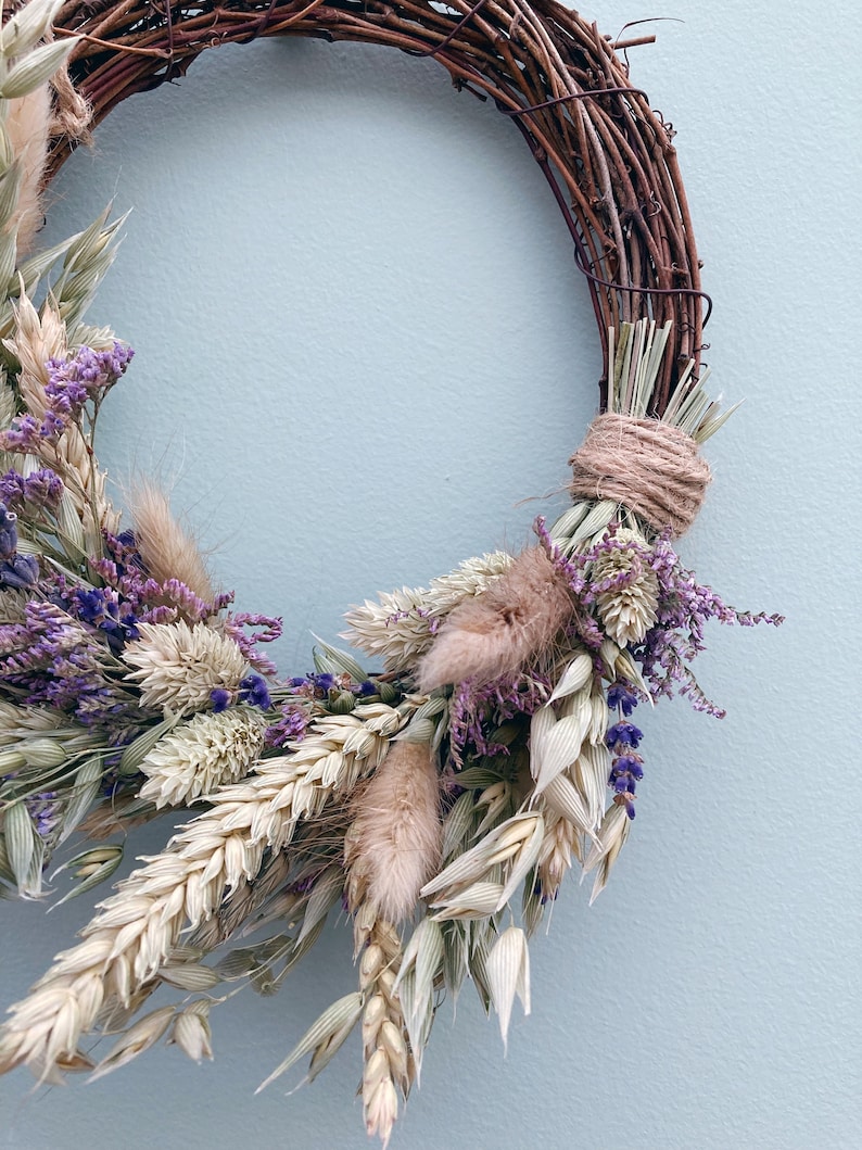 Op de afbeelding: Een krans van gedroogde bloemen met een bruine wijnstokbasis. De krans is versierd met gedroogde tarwe, haver, lavendel en andere gedroogde bloemen.