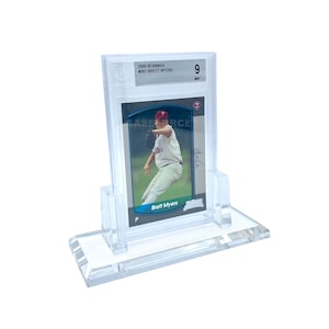May include: A clear acrylic display stand holding a baseball card. The card features a baseball player in a Phillies uniform. Text on the card reads "2000 Bowman #361 Brett Myers" and "Case Force". The card is graded as a 9.