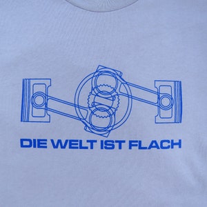 May include: A light blue t-shirt with a blue outline of a car engine and the text "DIE WELT IST FLACH" printed on the front.
