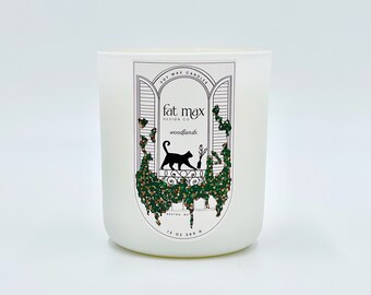 May include: White soy wax candle with a black cat illustration on the label. The label says "fat max design co" and "woodlands".