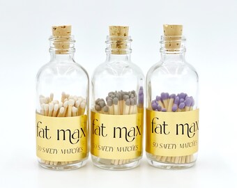 May include: Three glass bottles with cork stoppers filled with 50 safety matches. The matches have different colored tips: white, gray, and purple. Each bottle has a gold label with the text "fat max" and "50 safety matches".