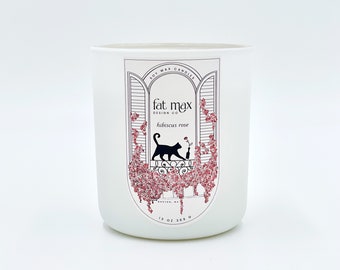 May include: A white soy wax candle with a black cat and pink flowers on the label. The label reads "fat max design co hibiscus rose".