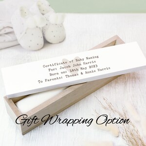 May include: A white wooden box with a brown lid. The lid has a certificate of baby naming for Jacob John Harris, born on 18th May 2023, to parents Thomas and Annie Harris. The box is a gift wrapping option.