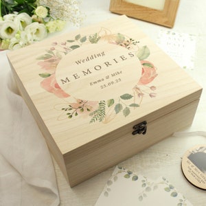 May include: A wooden box with a floral design and the text "Wedding Memories" on the lid. The box is decorated with a watercolour floral wreath and the names "Emma & Mike" and the date "23.09.23".