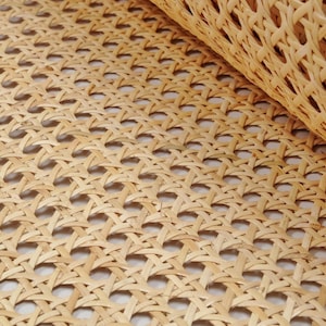 May include: Close-up of a woven cane webbing material, often used for chair seats and backs. The material is light brown and has a diamond pattern.
